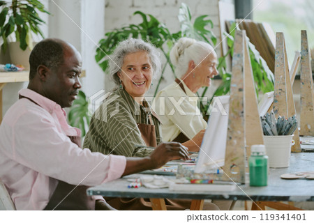 Retired biracial people having fun together while painting on canvas together in drawing studio 119341401