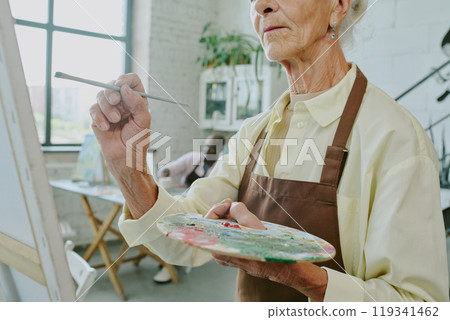 Low angle shot of unrecognizable senior woman holding dirty palette and paint brush while creating work of art on canvas 119341462