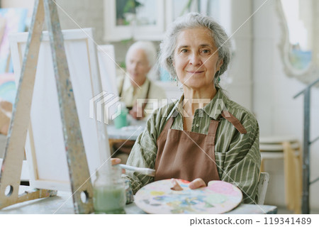 Portrait of calm senior woman demonstrating wooden palette with paints and paint brush Portrait of calm senior woman demonstrating wooden palette with paints and paint brush 119341489