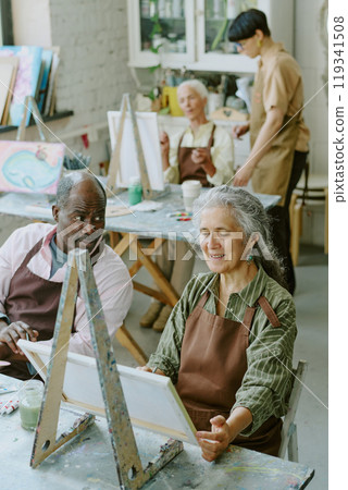 Vertical high angle shot of African American husband looking at his Caucasian wife with love while she painting on canvas Vertical high angle shot of African American husband looking at his Caucasian wife with love while she painting on canvas 119341508