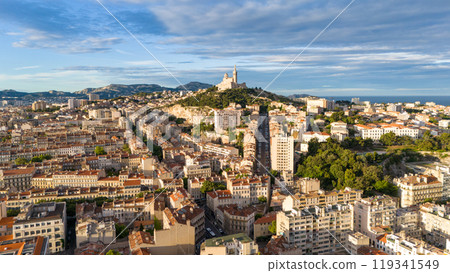 Aerial view of Marseille, France, featuring rooftops, streets, and the Notre-Dame de la Garde basilica, with the Mediterranean Sea in the background. Aerial view of Marseille, France, featuring rooftops, streets, and the Notre-Dame de la Garde basilica, with the Mediterranean Sea in the background. 119341549
