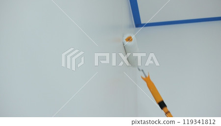 Man worker using roller to paint the walls in the house in white color. Room renovations at house. 119341812