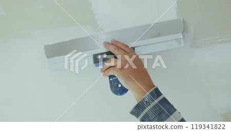 Plastering a concrete wall with putty using a large spatula. The master of apartment renovation levels the walls with starting plaster. The internal construction and finishing work. 119341822