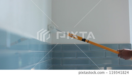 Man painter painting a house wall with a white paint roller. Painting and repair of the premises. Man painter painting a house wall with a white paint roller. Painting and repair of the premises. 119341824