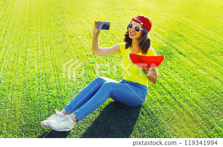 Summer happy young woman taking selfie with phone with watermelon on the grass in the summer park Summer happy young woman taking selfie with phone with watermelon on the grass in the summer park 119341994