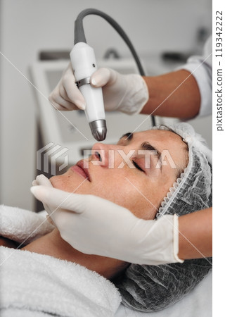 Woman receiving a facial treatment with a handheld device in a spa Woman receiving a facial treatment with a handheld device in a spa 119342222