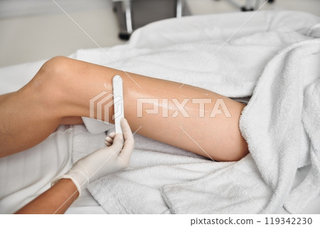 Waxing treatment on a clients leg in a clean salon setting in daylight Waxing treatment on a clients leg in a clean salon setting in daylight 119342230