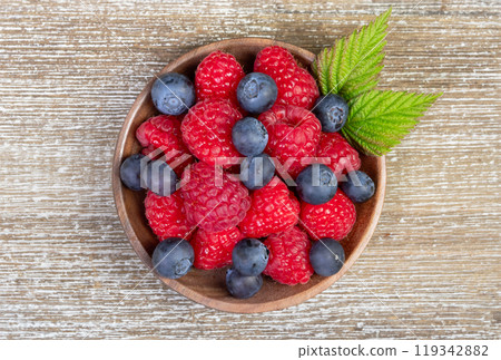 Plate with raspberries and blueberries with leaves on the wooden rustic table. 119342882