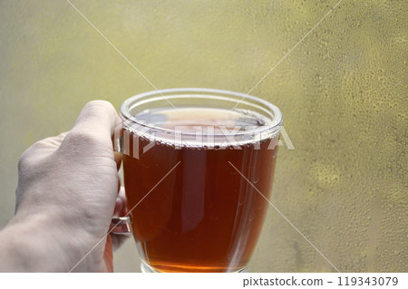 A cup of hot, aromatic tea in your hand against a condensation-covered window A cup of hot, aromatic tea in your hand against a condensation-covered window 119343079