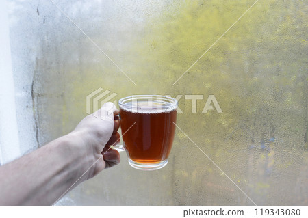 A cup of hot, aromatic tea in your hand against a condensation-covered window 119343080