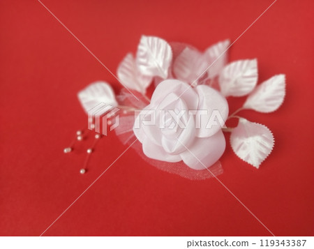 A stunning white rose stands out beautifully against a rich red background, complemented by soft leaves and small pearl accents, ideal for a wedding setting A stunning white rose stands out beautifully against a rich red background, complemented by soft leaves and small pearl accents, ideal for a wedding setting 119343387