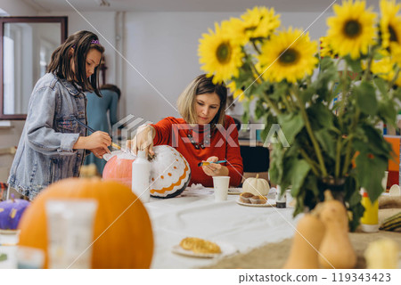 Children and adults painting pumpkins for Halloween, enjoying a fun and creative activity together. 119343423