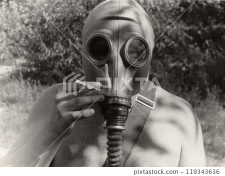 Vintage photo of a soldier in a gas mask without clothes. Humor. The man is holding a cigarette in his hand. Vintage photo of a soldier in a gas mask without clothes. Humor. The man is holding a cigarette in his hand. 119343636