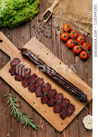 Smoked salami sticks on a wooden board with herbs, perfect for charcuterie boards and gourmet snacks 119344265
