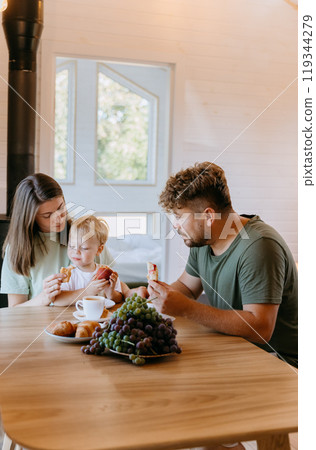 Family enjoying breakfast together with croissants, grapes, and coffee in a cozy home atmosphere 119344279