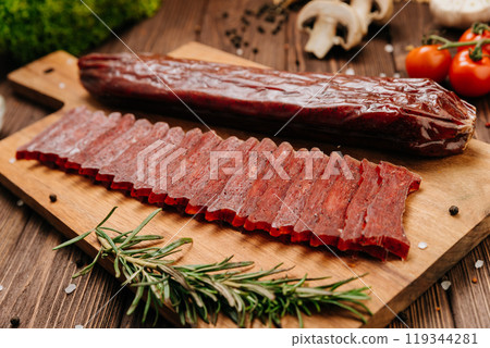 Sliced gourmet smoked salami on a wooden board with herbs, perfect for charcuterie boards and snacks Sliced gourmet smoked salami on a wooden board with herbs, perfect for charcuterie boards and snacks 119344281