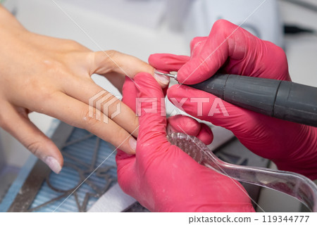 Nail technician carefully applies a nail drill for a detailed hardware manicure on a clients nails in the salon. Nail technician carefully applies a nail drill for a detailed hardware manicure on a clients nails in the salon. 119344777