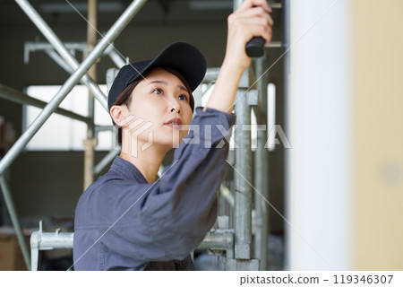 A female craftsman applying paint to plasterboard with a trowel 119346307
