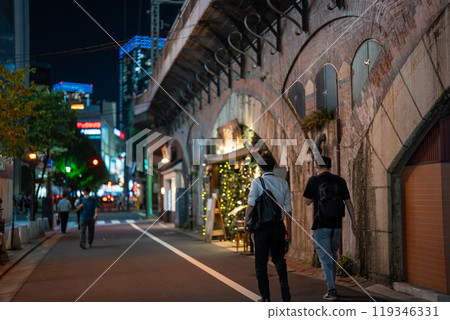A view of Tokyo at night under a railway overpass. Photographing restaurant food, office workers returning home from work, and other people's backs. 119346331