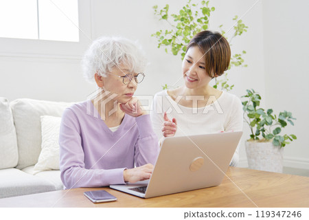 Daughter teaching her mother how to use a laptop in the living room 119347246