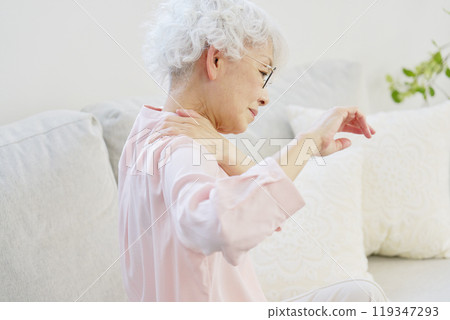 Back view of a senior woman with stiff shoulders in the living room 119347293