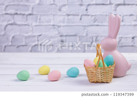 Easter composition with a pink rabbit figurine and a basket with candies. Easter composition with a pink rabbit figurine and a basket with candies. 119347399