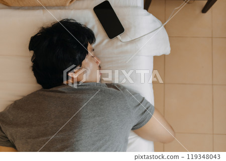 Close up face of sleepy man slept with his mobile phone left near his head. 119348043