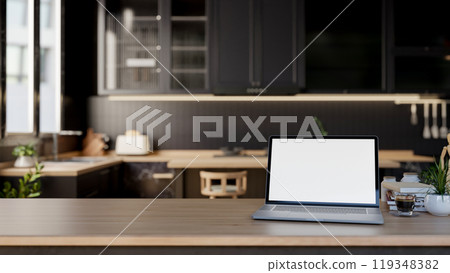 A close-up of a laptop mockup on a wooden kitchen tabletop in a modern, luxurious black kitchen. 119348382
