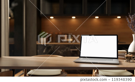 A close-up of a laptop mockup on a hardwood dining table in a contemporary, luxurious kitchen. 119348390