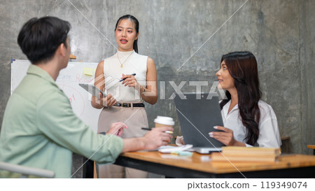 A confident and professional Asian businesswoman is speaking during a meeting with her team. 119349074