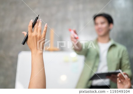 A businesswoman raising her hand to ask a question or share her ideas during a meeting with her team A businesswoman raising her hand to ask a question or share her ideas during a meeting with her team 119349104