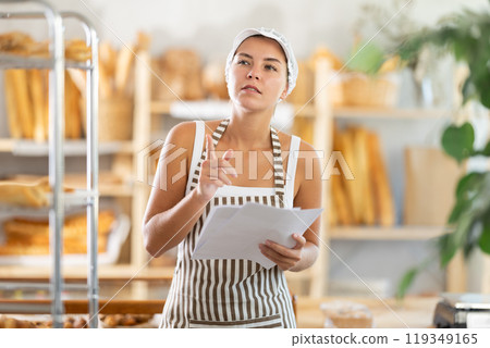 Young woman seller reading document in bakery Young woman seller reading document in bakery 119349165