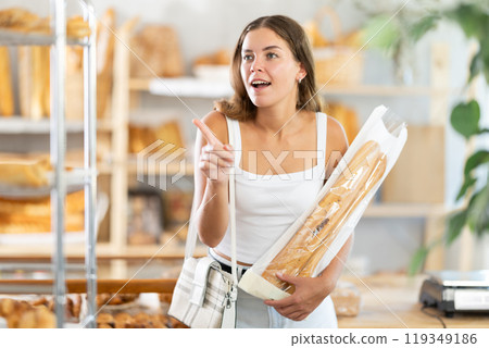 Young woman holding baguettes looks around the bakery 119349186