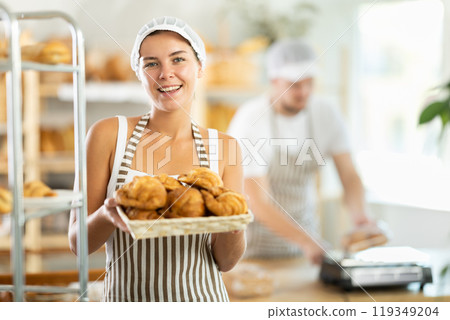 Young saleswoman displays croissants in square wicker basket 119349204