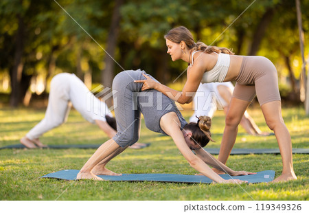 Woman doing Downward Facing Dog Pose with yoga instructor Woman doing Downward Facing Dog Pose with yoga instructor 119349326