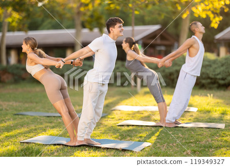 Young couple performing trust-building pose during partner yoga outdoors 119349327