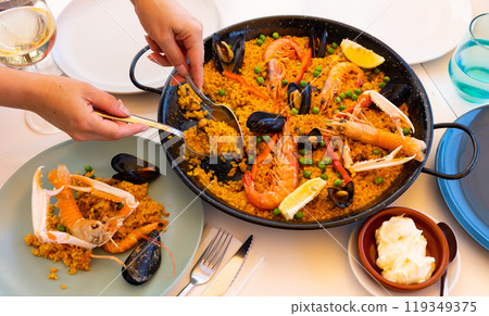 Womens hands lay out sea paella in plates for family dinner 119349375