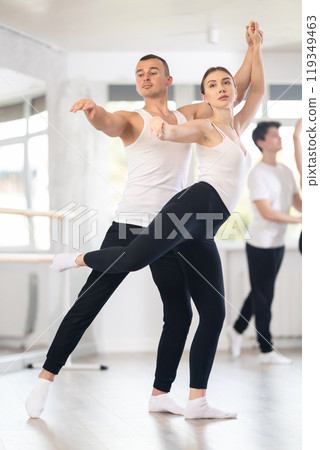 Happy young caucasian man and woman practicing ballet arabesque pose in ballroom 119349463