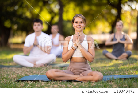 Yoga lesson visitors with girl coach perform padmasana in park 119349472