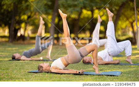 Yoga lesson visitors with coach perform Setu Badha Sarvangasana in park Yoga lesson visitors with coach perform Setu Badha Sarvangasana in park 119349475
