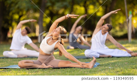 Yoga lesson visitors with coach perform Parivritta Janu Shirshasana in park 119349595