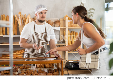 Young man seller serves girl buying fresh croissants in bakery 119349599