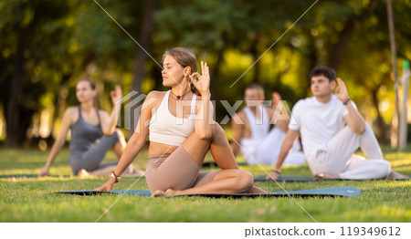 Yoga lesson visitors with coach perform Matsyendrasana in park Yoga lesson visitors with coach perform Matsyendrasana in park 119349612