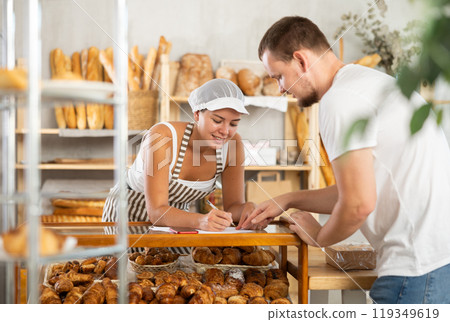 Positive woman worker and a man write on sheets of paper by the croissants display Positive woman worker and a man write on sheets of paper by the croissants display 119349619