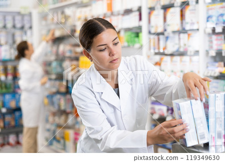 Young female pharmacist arranges product in pharmacy 119349630