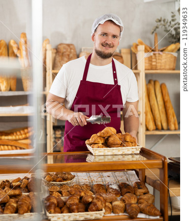 Young man seller puts croissants in showcase Young man seller puts croissants in showcase 119349633