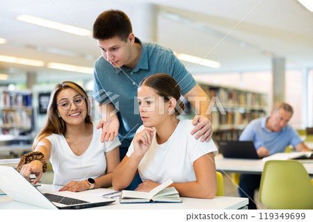 Young male librarian giving advice to positive female students using laptop in the library Young male librarian giving advice to positive female students using laptop in the library 119349699