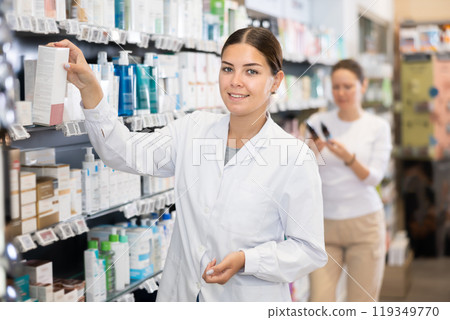 In chemist s shop, woman consultant designs showcase with beauty care cosmetics In chemist s shop, woman consultant designs showcase with beauty care cosmetics 119349770