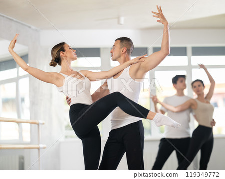 Happy smiling woman dressed in black and white sportswear enjoying ballet choreography with male partner during group class in dance salon Happy smiling woman dressed in black and white sportswear enjoying ballet choreography with male partner during group class in dance salon 119349772