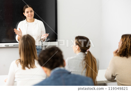 Positive female trainer standing near interactive board and conducting advanced training courses to office employees sitting at desks in classroom 119349821